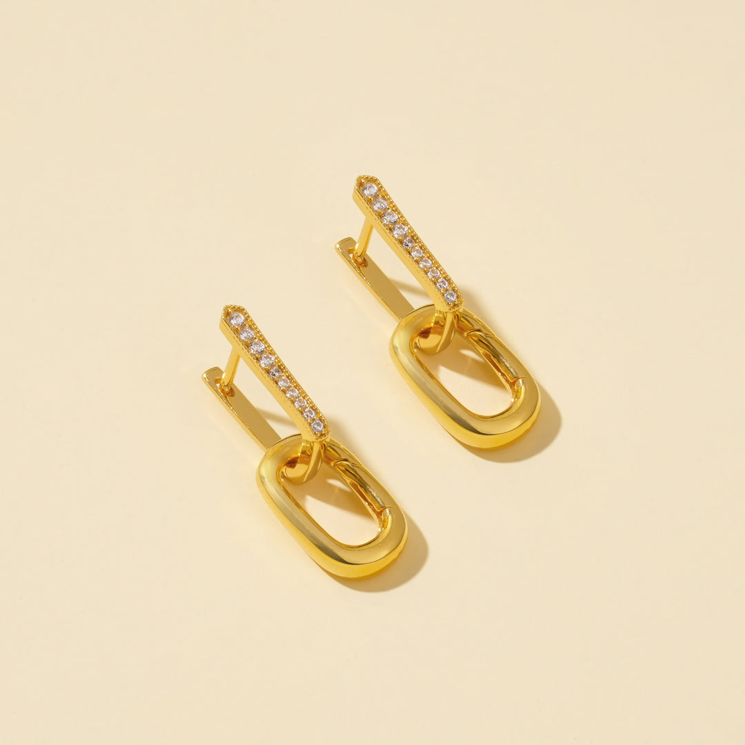 Gold earrings with diamond accents on a beige background