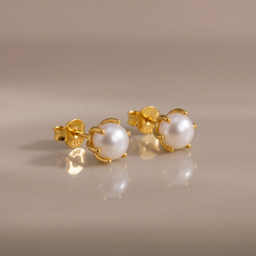 Gold earrings with pearl studs on a beige background