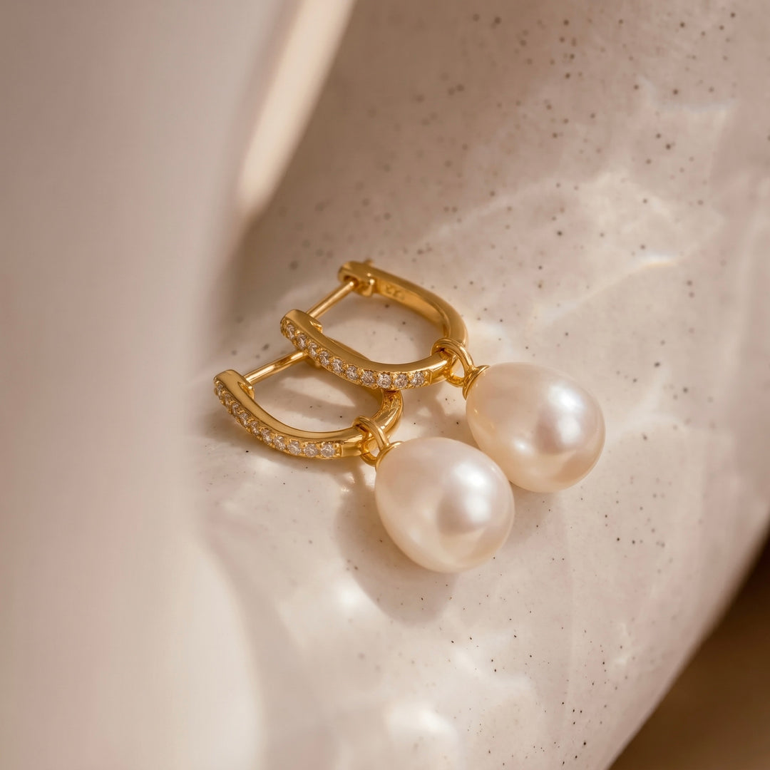 Gold earrings with pearls on a textured beige surface