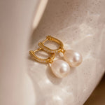 Load image into Gallery viewer, Gold earrings with pearls on a textured beige surface
