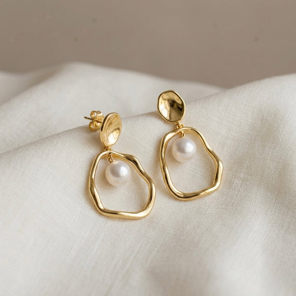 Gold earrings with pearls on a white fabric background