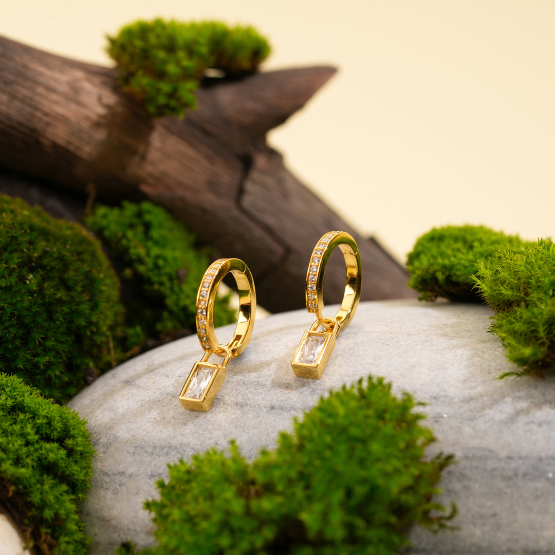 Gold hoop earrings with diamond accents on a stone surface surrounded by greenery