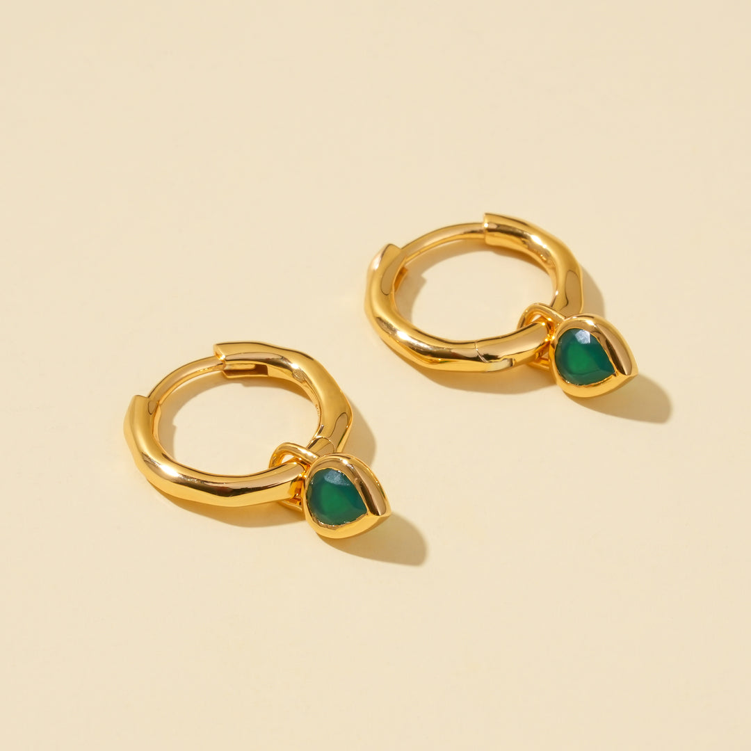 Gold hoop earrings with green stones on a beige background