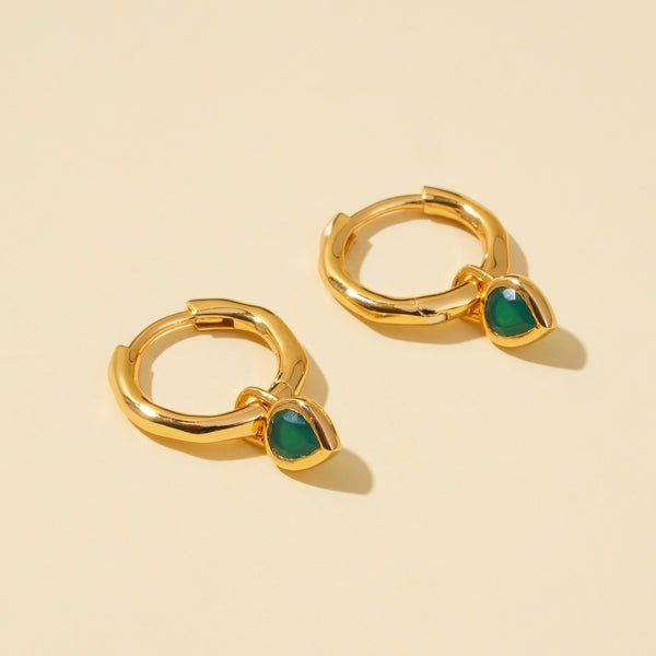 Gold hoop earrings with green stones on a beige background