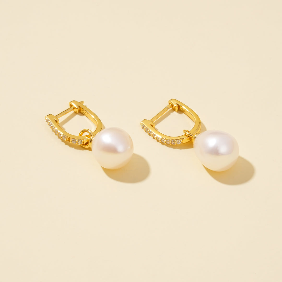Gold hoop earrings with pearl drops on a beige background