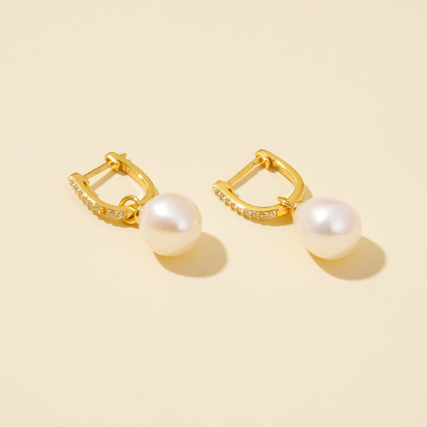 Gold hoop earrings with pearl drops on a beige background