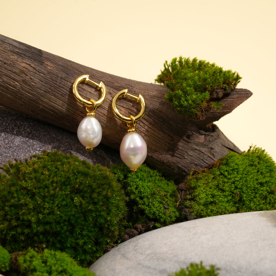 Gold hoop earrings with pearls on a natural background of wood and moss.