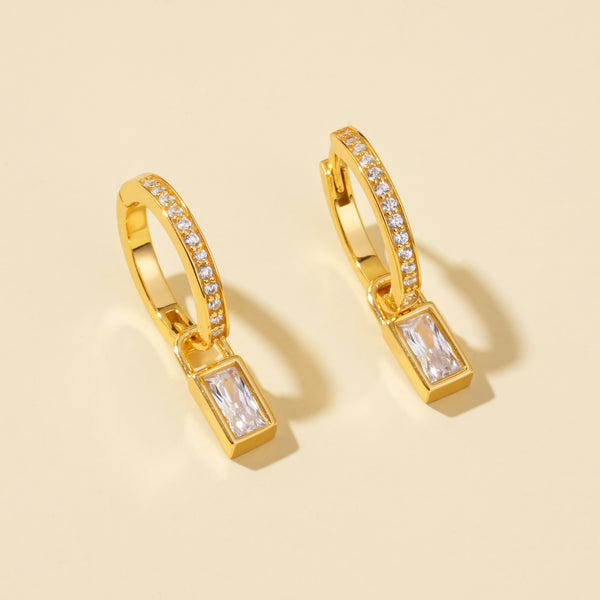 Gold hoop earrings with rectangular gemstones on a beige background