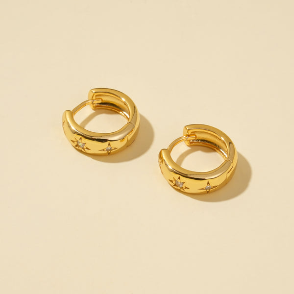 Gold hoop earrings with star and moon designs on a beige background