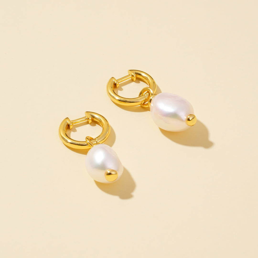 Gold hoop earrings with white pearls on a beige background