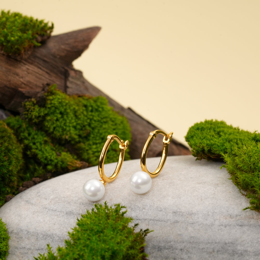 Gold hoop earrings with white pearls on a stone surface with green moss.