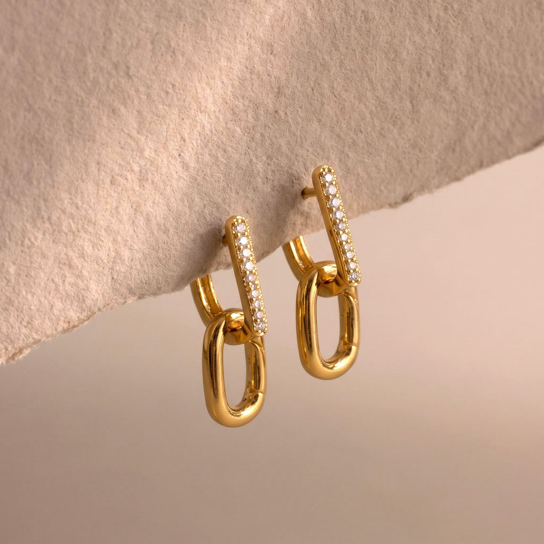 Gold hoop earrings with embedded stones on a beige stone surface