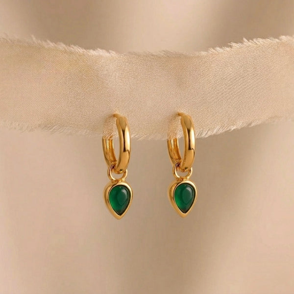 Gold hoop earrings with green gemstones on a beige fabric background