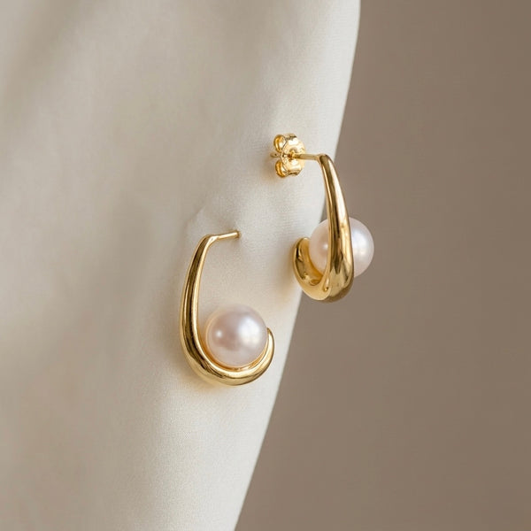 Gold hoop earrings with pearl centers on a neutral background