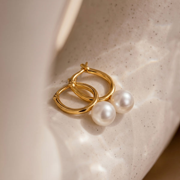 Gold hoop earrings with pearls on a textured beige surface
