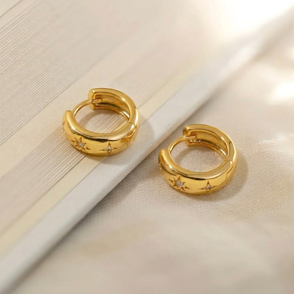 Gold hoop earrings with star designs on a light background
