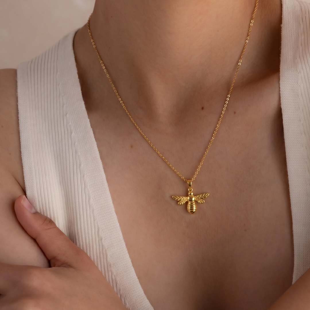 Gold necklace with a bee pendant worn by a person in a white top.