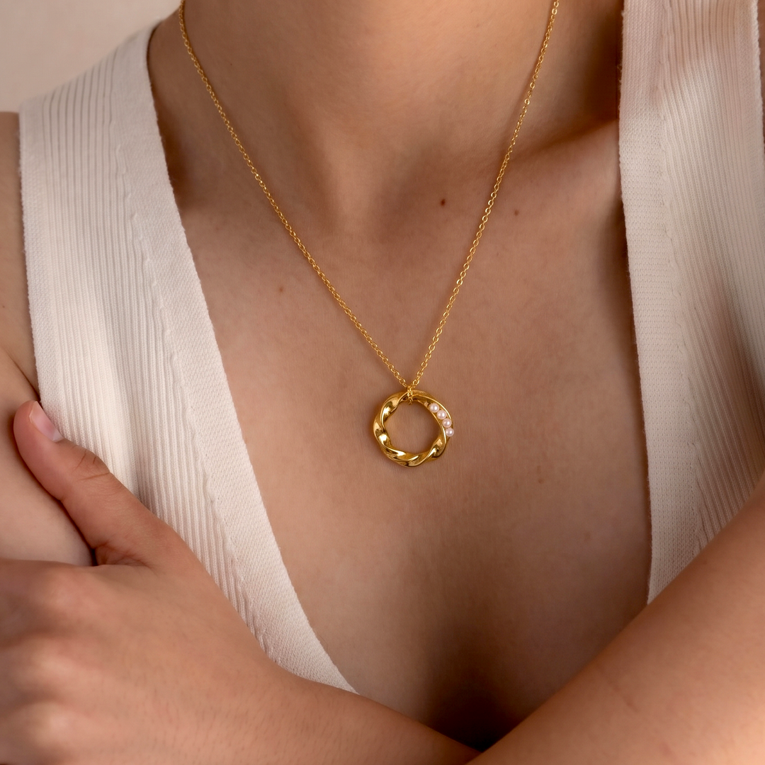 Gold necklace with a circular pendant worn by a person in a white top.