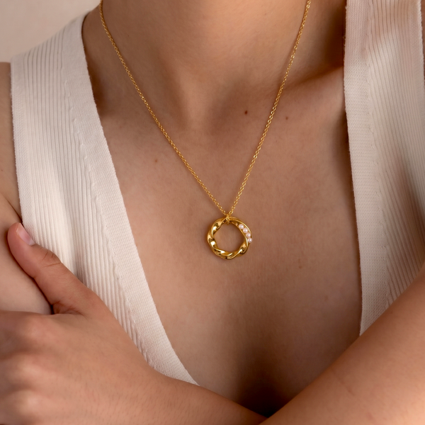 Gold necklace with a circular pendant worn by a person in a white top.