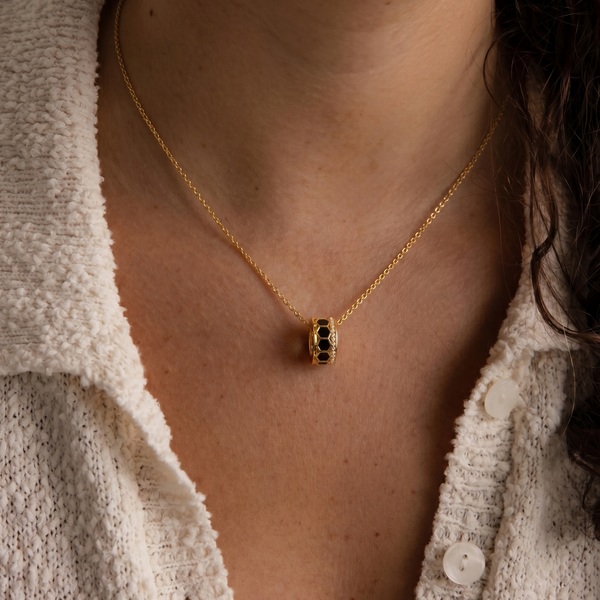 Gold necklace with a hexagonal pendant worn by a person in a textured white cardigan.