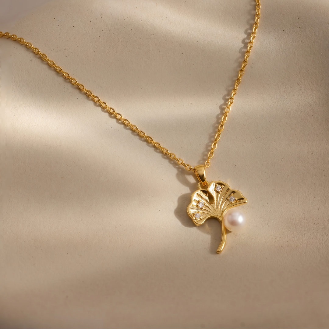 Gold necklace with a leaf-shaped pendant on a beige background