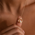 Load image into Gallery viewer, Gold necklace with a pearl pendant held by a hand against a brown background
