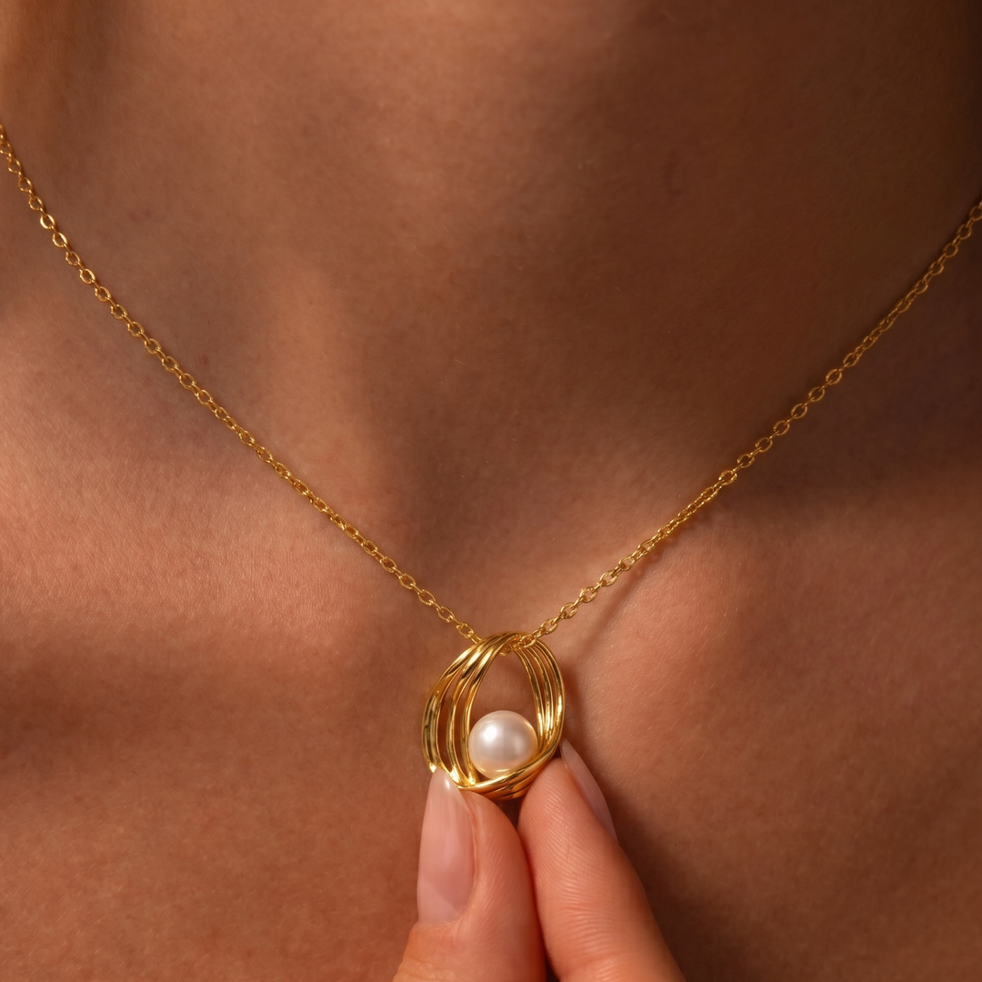 Gold necklace with a pearl pendant held by a hand against a skin-toned background