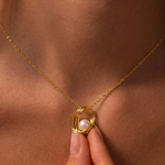 Load image into Gallery viewer, Gold necklace with a pearl pendant held by a hand against a skin-toned background
