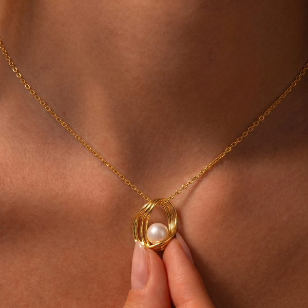 Gold necklace with a pearl pendant held by a hand against a skin-toned background