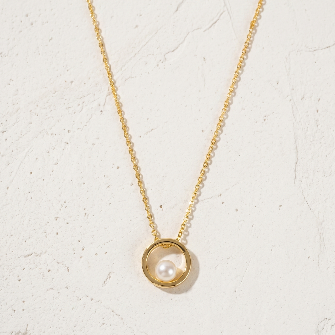 Gold necklace with a pearl pendant on a light beige background