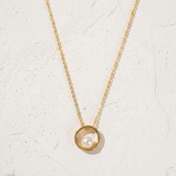Gold necklace with a pearl pendant on a light beige background