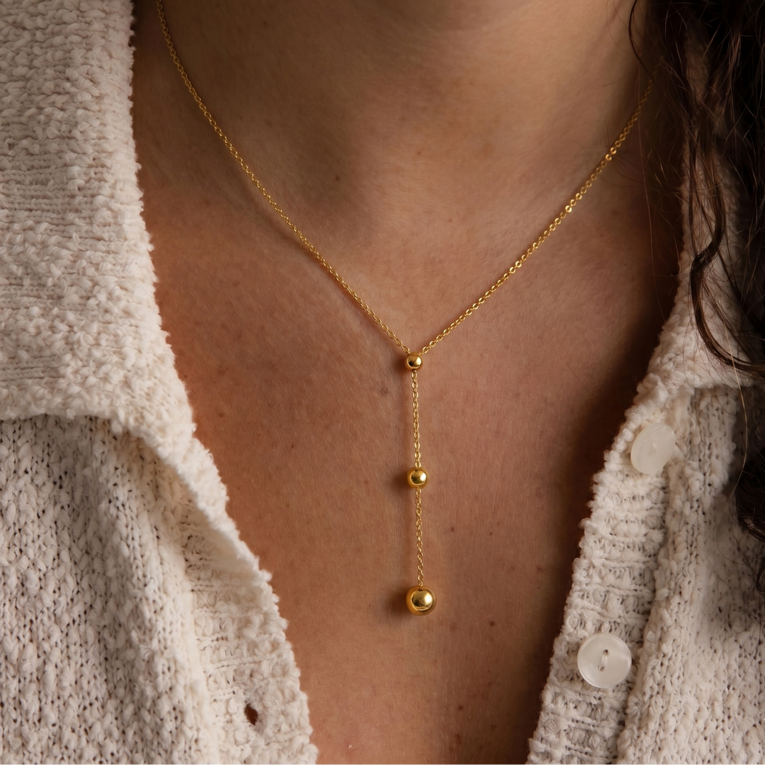Gold necklace with a pendant worn by a person in a textured white cardigan.
