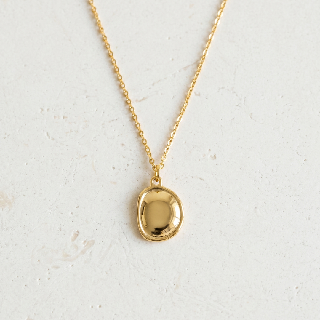 Gold necklace with a round pendant on a light gray background