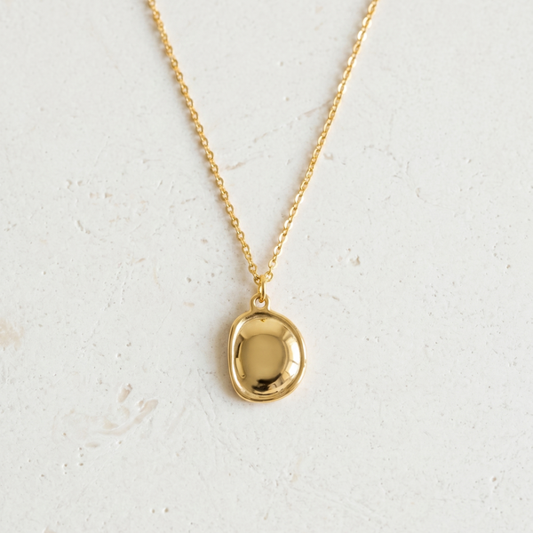 Gold necklace with a round pendant on a light gray background