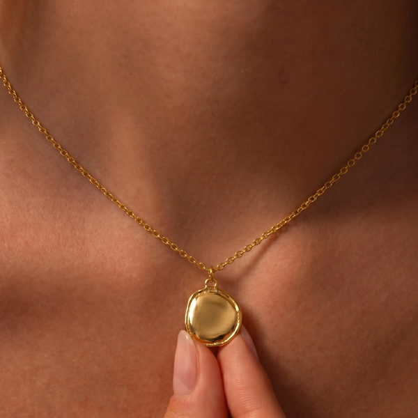Gold necklace with a round pendant on a person's neck
