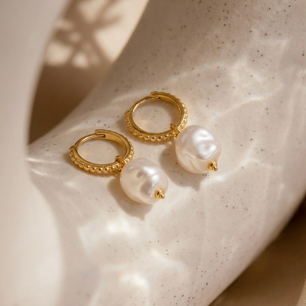 Gold hoop earrings with pearls on a textured beige surface