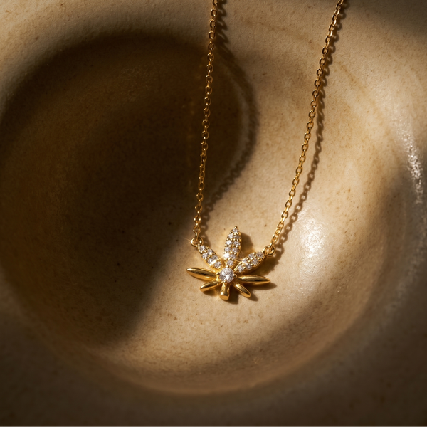 Gold plated necklace with a leaf-shaped pendant on a textured surface