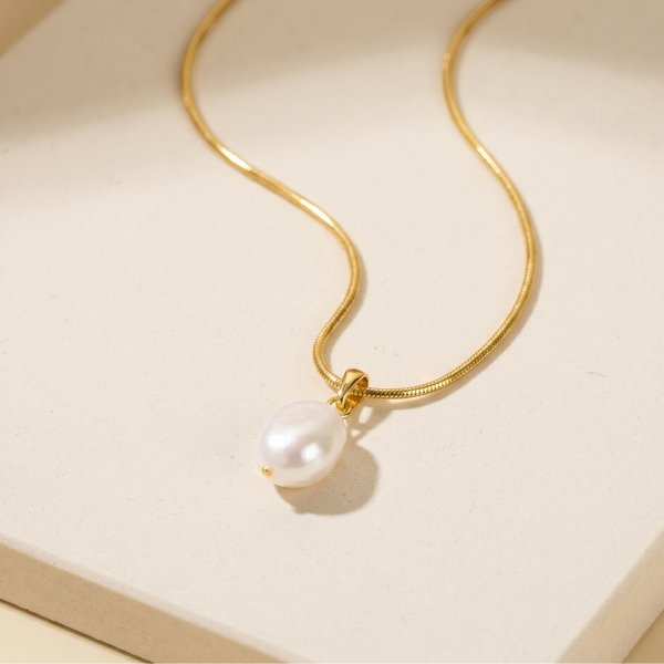 Gold plated necklace with a pearl pendant on a beige background