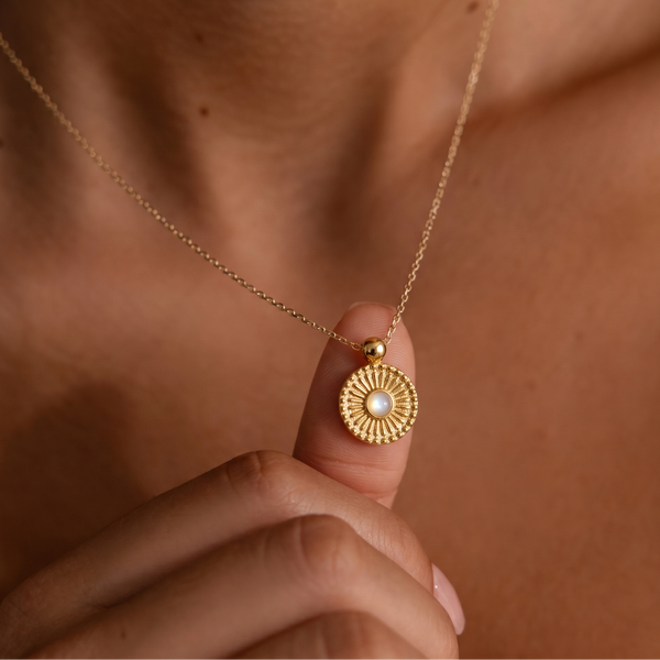Gold plated necklace with a pendant held by a hand against a brown background