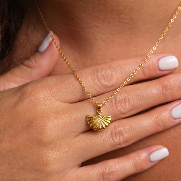 Gold plated necklace with a shell pendant worn by a person