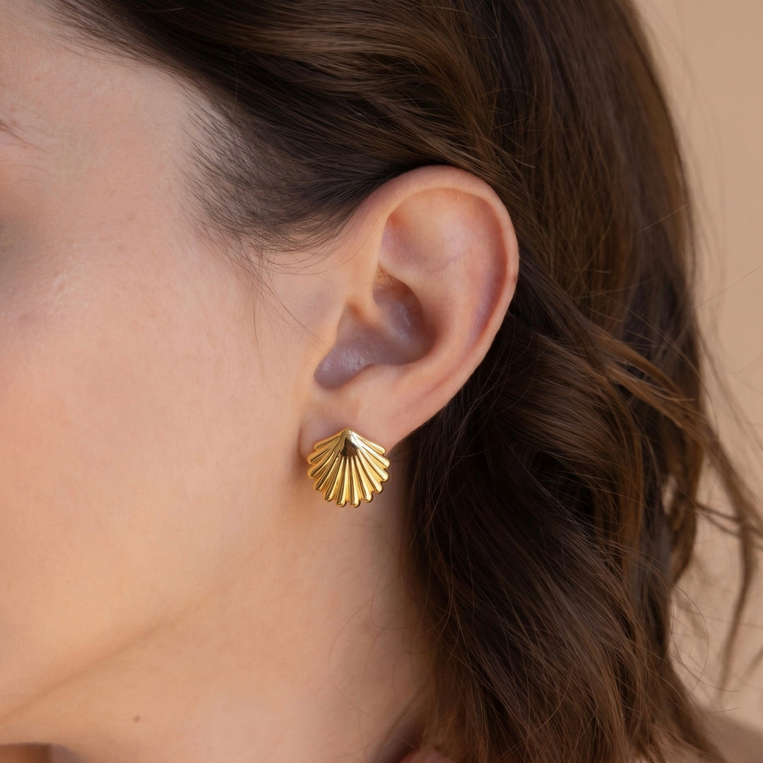 Gold shell-shaped earring worn by a person with brown hair.