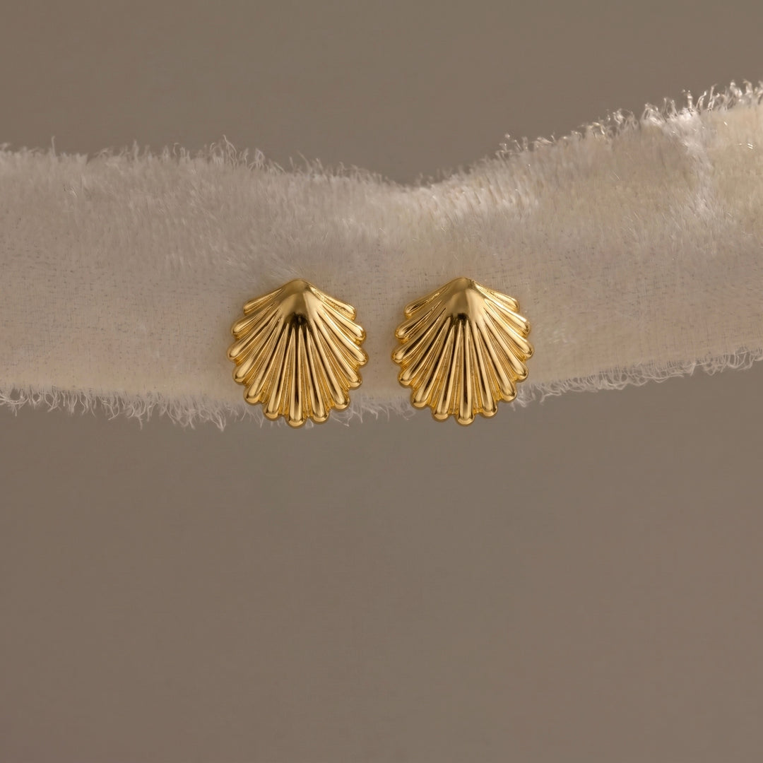Gold shell-shaped earrings on a beige fabric background