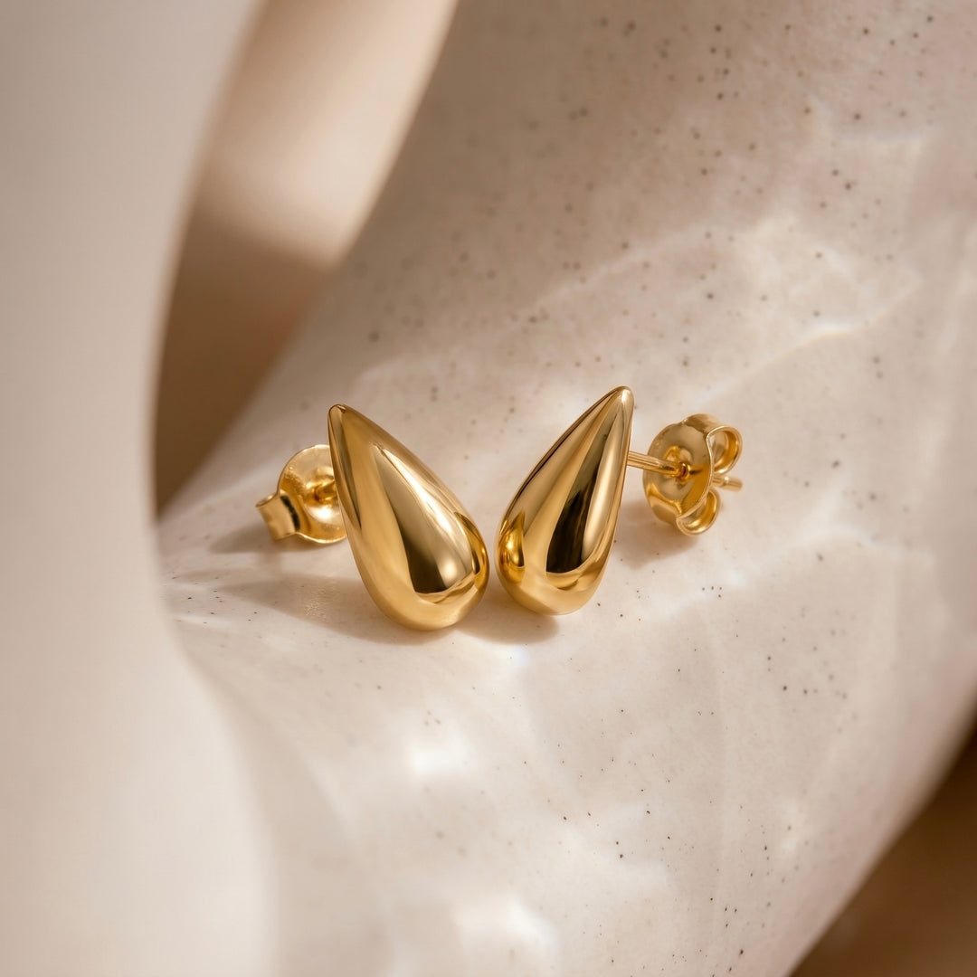 Gold teardrop earrings on a speckled beige surface