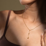 Load image into Gallery viewer, A close-up of a model wearing an elegant gold lariat necklace from Zewory Jewellery. The delicate Y-necklace features a drop chain with two polished gold beads that rest gracefully on her chest, showcased against her brown top.
