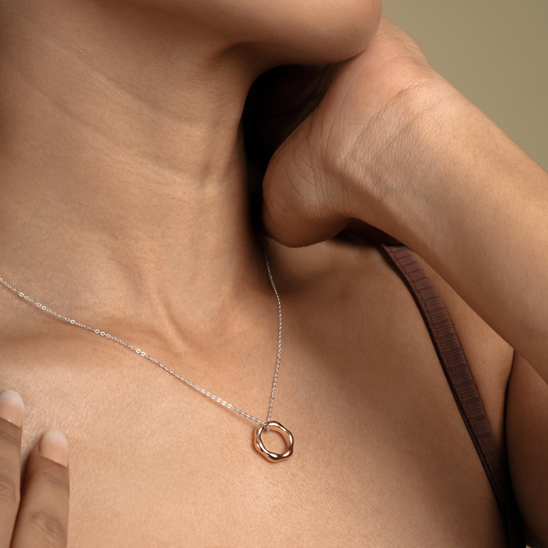 A close-up of a model wearing a chic two-tone necklace from Zewory Jewellery. The delicate silver chain is complemented by an organic, irregular-shaped rose gold circle pendant, creating a modern mixed-metal look against her skin.