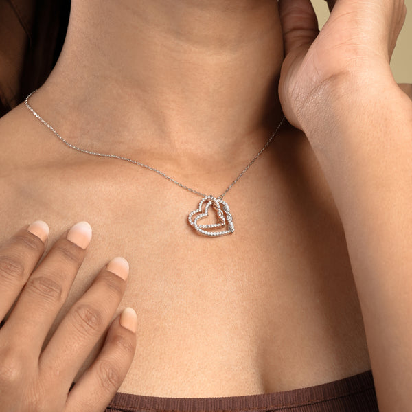 A close-up of a model wearing a sparkling two-tone interlocking hearts necklace from Zewory Jewellery. The romantic pendant, featuring silver and rose gold hearts covered in pavé crystals, rests elegantly against her skin, making it an ideal anniversary or special occasion gift.