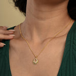 Load image into Gallery viewer, A close-up of a model wearing a radiant gold sun necklace from Zewory Jewellery. The celestial pendant, featuring faceted sun rays and a sparkling crystal-lined center, rests elegantly on her skin against her dark green top.
