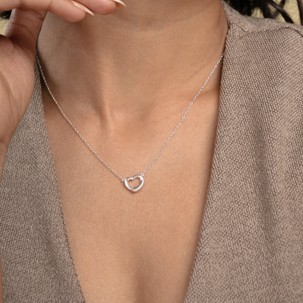 A close-up of a model wearing a delicate silver open heart necklace from Zewory Jewellery. The minimalist, polished heart pendant rests elegantly against her skin, showcasing a timeless and romantic accessory perfect for everyday wear.