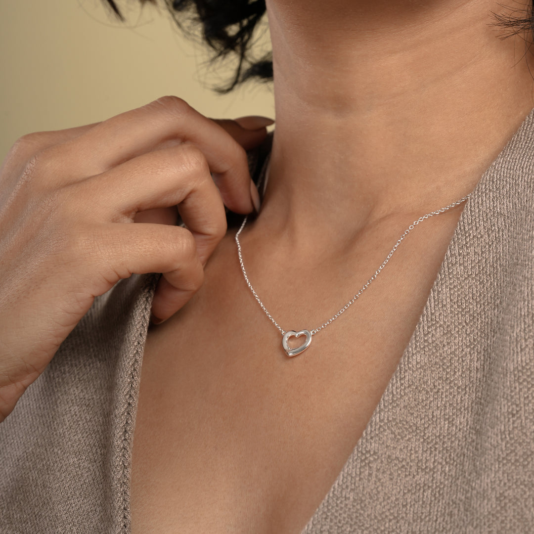 A close-up of a model wearing a delicate silver open heart necklace from Zewory Jewellery. The minimalist, polished heart pendant rests elegantly against her skin, showcasing a timeless and romantic accessory perfect for everyday wear.
