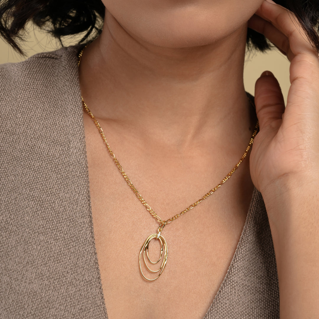  A close-up of a model wearing a modern gold statement necklace from Zewory Jewellery. The elegant figaro chain leads to a triple oval hoop pendant with a sparkling crystal accent, showcased beautifully against her neutral-coloured top.